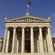 The Academy of Athens features a Greek flag flying over a monumental building with columns, a cornice and statues